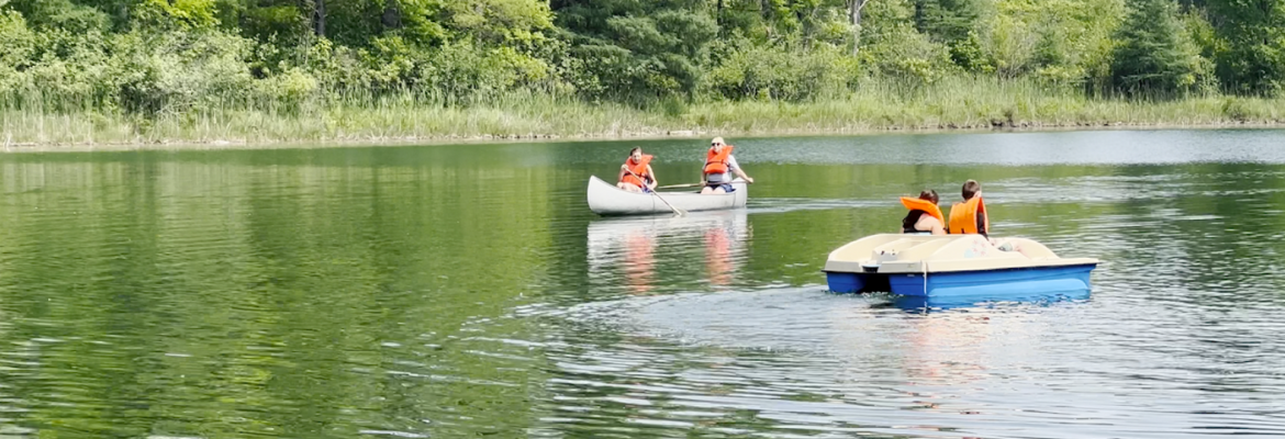 Two people paddle in a canoe on Lake Flannigan on a sunny summer day while another pair navigates the lake in a paddle boat.