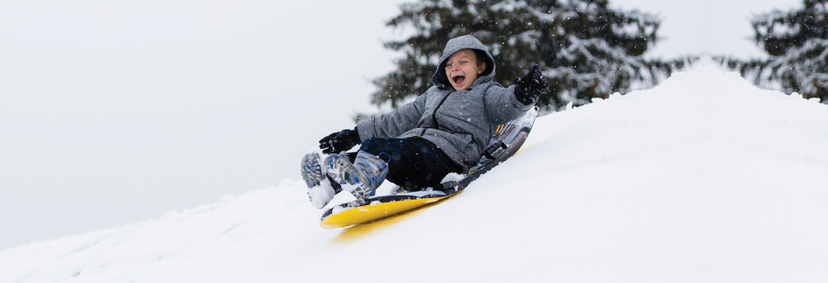 A young boy laughs while sledding downhill on a snowy day.