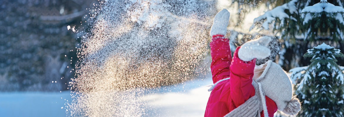 A child throws her hands up in the air while playing in the snow on a sunny day.