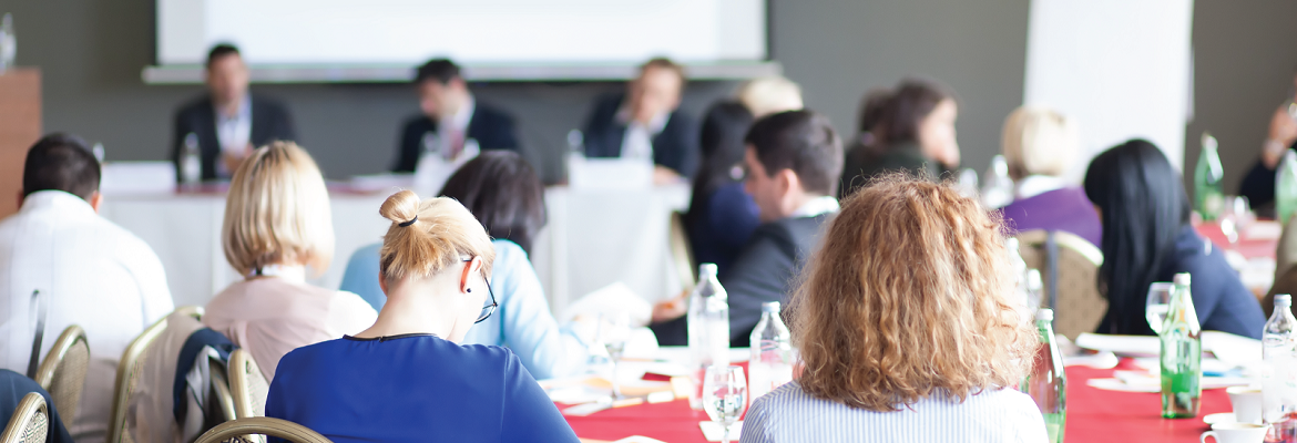 Conference attendees take notes while listening to a presenter.