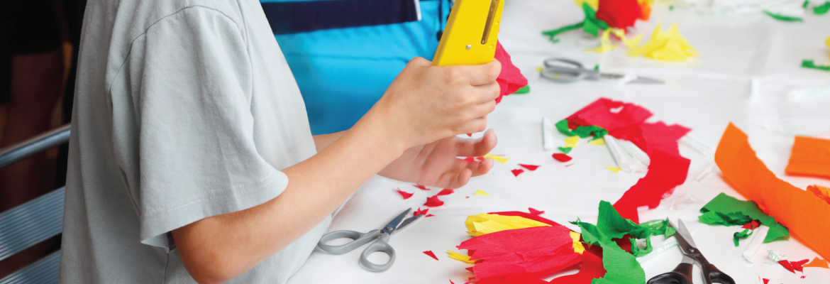 Closeup of someone doing a craft project with bright tissue paper and a stapler.