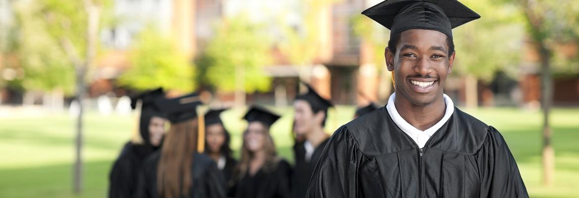 A male student smiles at the camera while wearing a black cap and gown for graduation.