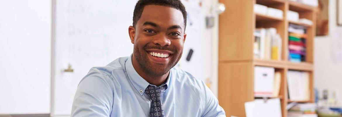 A man wearing a button-down shirt and tie smiles at the camera.