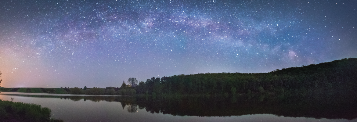 A star-filled night sky over a tree-lined lake.