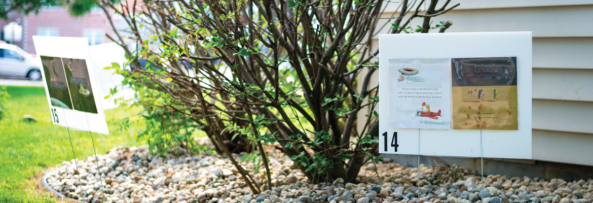 Two signs featuring pages of a book are placed low to the ground next to a building.