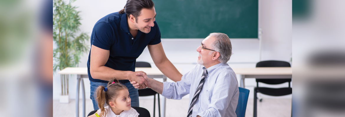 A little girl smiles as her smiling dad leans down to shake hands with a seated teacher at school.