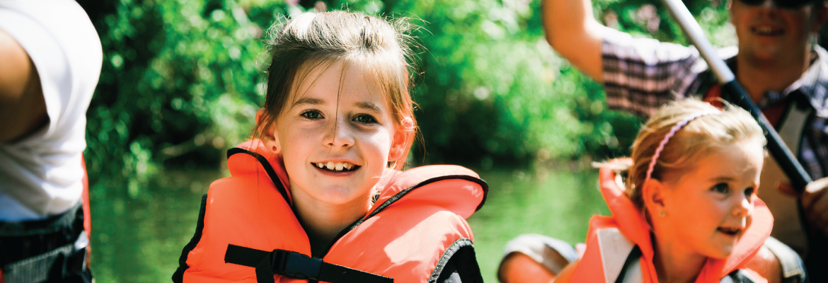 Two young girls wear life jackets while in a canoe with their parents.