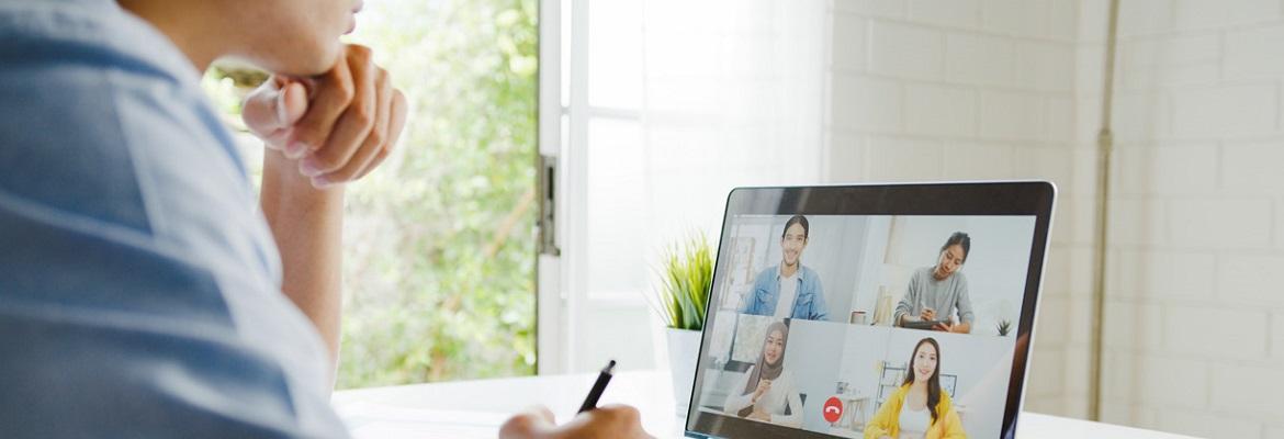 View over the shoulder of someone who is taking notes while in a video call with four other people.