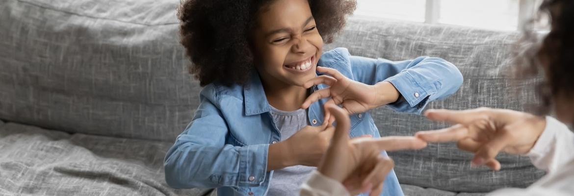 A child smiles while communicating in sign language with an adult.