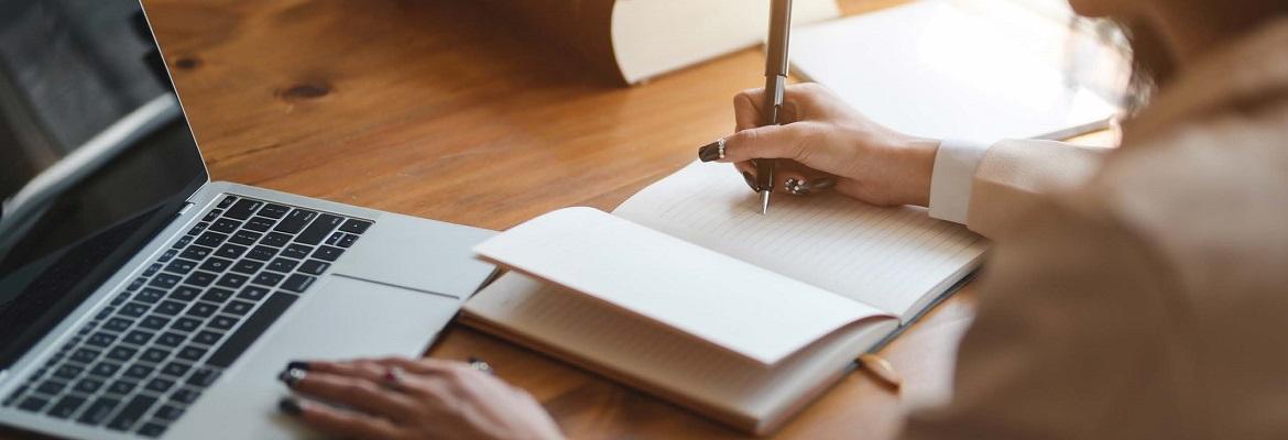 Closeup of a woman taking notes while sitting in front of an open laptop.