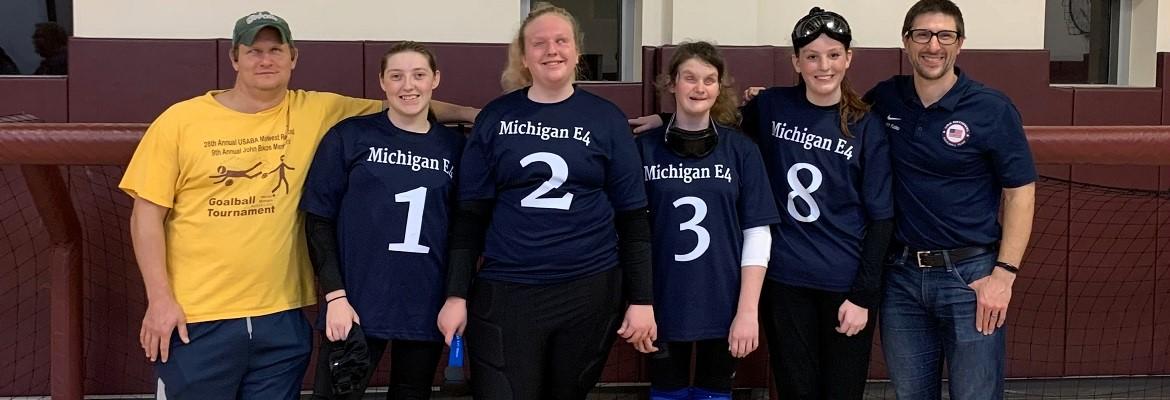 A group photo featuring four members of the girls' Michigan goalball team wearing their uniforms, along with their two coaches.