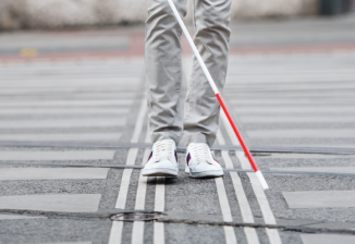 A person crossing a street and using a white cane.
