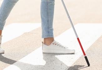 Closeup of someone's legs as they walk across a crosswalk with a white cane.