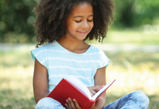 A young girl reading a book outside on a sunny day. 