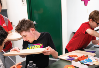 A group of student sit around a table doing a craft activity at Camp T. 