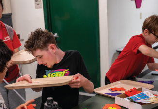 A group of student sit around a table doing a craft activity at Camp T. 