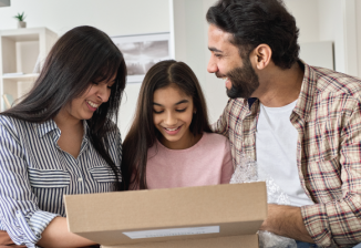 A family smiles as they open a brown shipping box. 