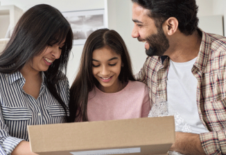 A family smiles while opening a brown shipping box. 