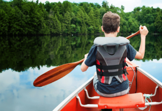 A young boy maneuvers a canoe on a tranquil lake, embraced by stunning scenery.