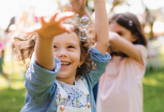 Young kids run and smile outside on a sunny day. 