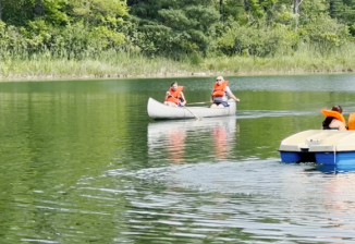 Two people paddle in a canoe on Lake Flannigan on a sunny summer day while another pair navigates the lake in a paddle boat.