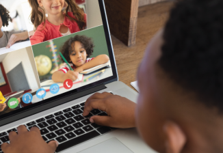 View over the shoulder of a young boy in a video call with several other children.