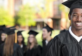 A male student smiles at the camera while wearing a black cap and gown for graduation.