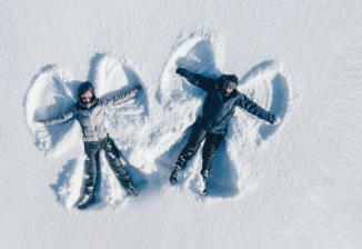 Overhead view of two children making snow angels in the snow by lying down and waving their arms and legs.