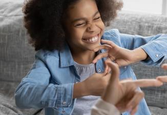 A child smiles while communicating in sign language with an adult.