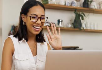 A woman smiles while waving in a video call.